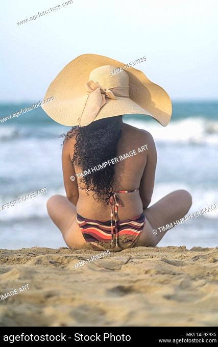 North America, Caribbean, Greater Antilles, Hispaniola Island, Dominican Republic, Puerto Plata Province, Cabarete, Attractive woman sitting on the beach and...