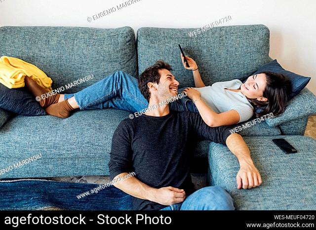 Happy girlfriend with smart phone looking at boyfriend at home