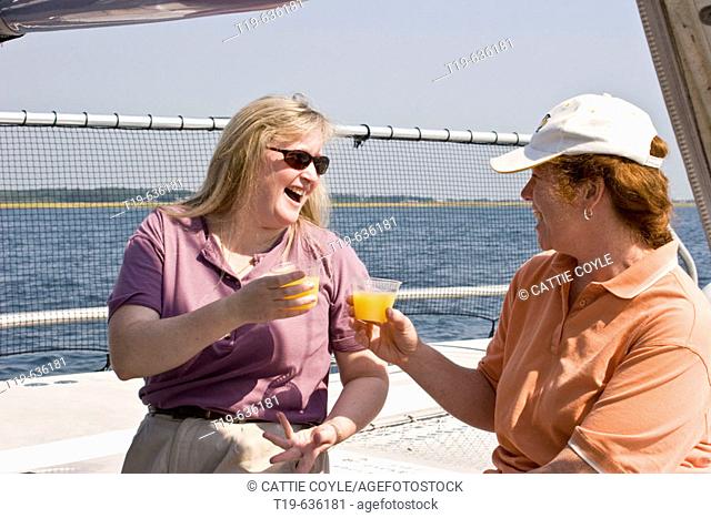 Two women on a 'girls day out' toasting with Mimosas (champagne & orange juice) on a catamaran outside Newburyport, MA, on a September afternoon. USA