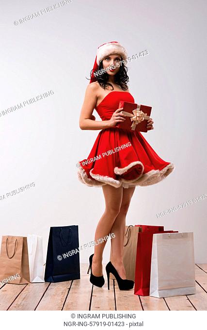 Sexy girl wearing Santa Claus clothes - dress and hat standing with Christmas gifts. Full length portrait