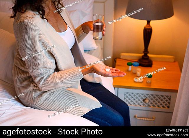 Mid section of senior caucasian woman in bedroom sitting on bed, holding pills