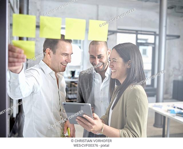 Happy colleague with sticky notes and tablet in office