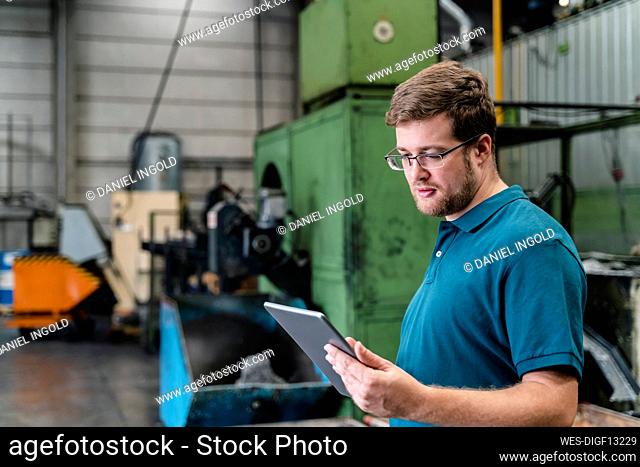 Male factory worker using digital tablet while standing in manufacturing industry