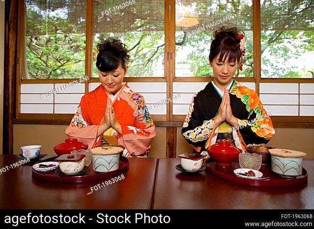 Young women in kimonos praying over lunch in restaurant