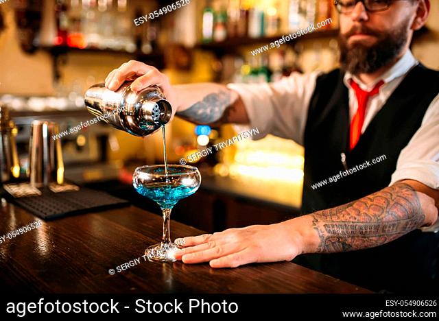 Bartender with shaker making alcohol cocktail behind a bar counter