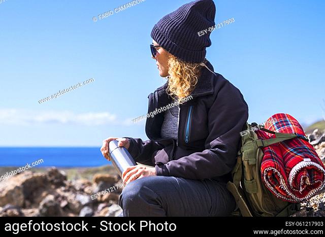 Active adult lady resting and taking a break while do trekking adventure activity inthe nature. Woman sit down on the rocks admiring ocean blue view