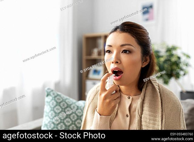 sick asian woman using oral spray medicine at home