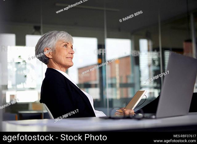 Senior businesswoman sitting at desk in office looking at distance