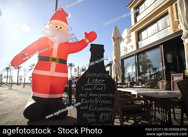 11 December 2023, Spain, Palma: An inflatable Santa Claus stands on the terrace of the ""Munchner Kindl"" restaurant on Arenal beach on a sunny day with a...