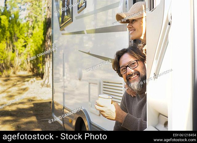Mature man and woman outside the door of a modern camper van motor home parked in the forest. Concept of travel and vacation with rented vehicle