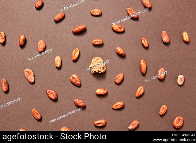 Piece of fresh natural cocoa mass in the middle of food pattern from cacao beans on a brown background, copy space. Top view