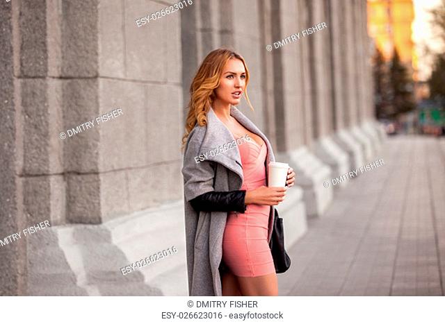 A pretty woman with a coffee to go against urban scene