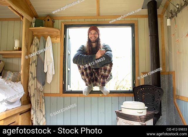Portrait happy young man in pajamas in tiny cabin window