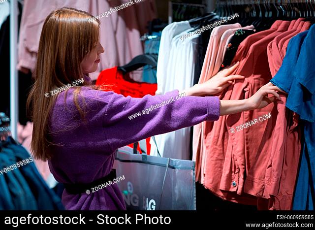 Young woman chooses clothes in shop store