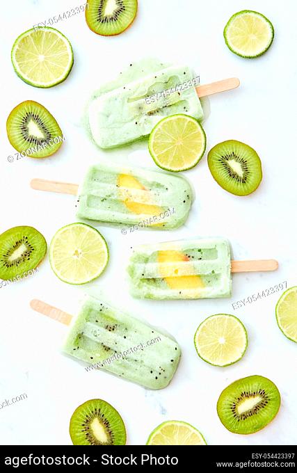 Summer pattern of frozen lime kiwi juice on a stick with a piece of peach and pieces of fruit on a gray background. Healthy dessert. Flat lay