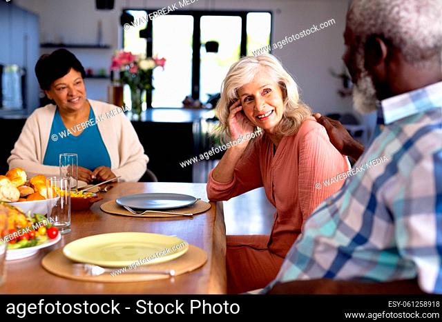 Happy multiracial senior friends with food on dining table talking while sitting in nursing home
