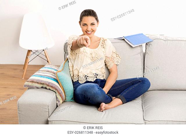 Beautiful woman sitting on the couch and pointing to the camera