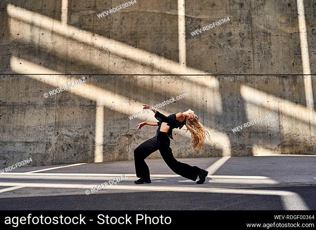 Carefree blond woman dancing on street by wall