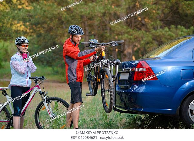 Young Couple Preparing for Riding the Mountain Bikes in the Forest. Unmounting the Bike from Bike Rack on the Car. Adventure and Family Travel Concept
