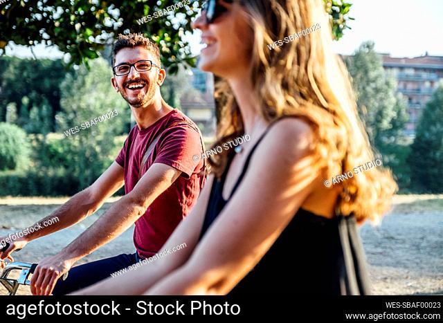 Cheerful mid adult man looking at girlfriend while riding bicycle in park