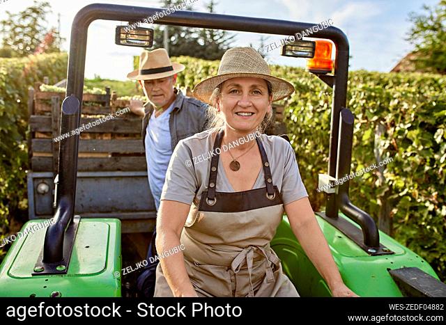 Mature farmers on tractor with crate of grapes in vineyard