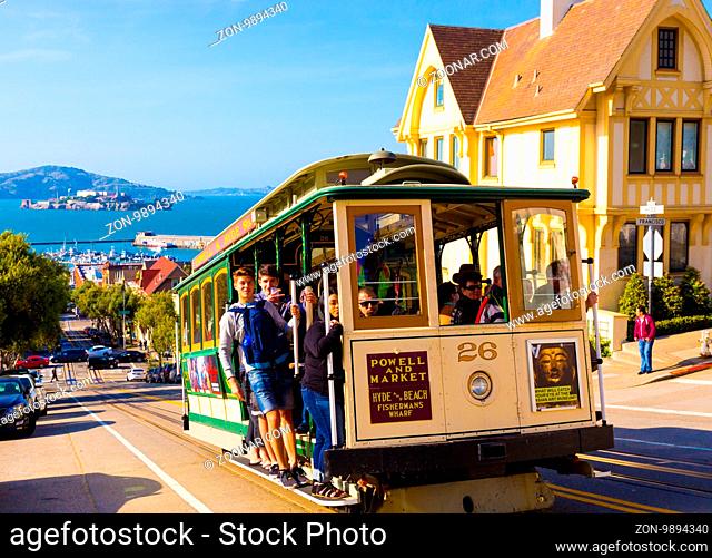 San Francisco, USA - May 12, 2016: Closeup of approaching Hyde Street cable car full of people standing on outside platform enjoying steep hill ride with...