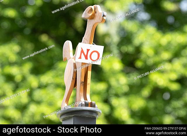 02 June 2020, Saxony, Bad Schandau: A wooden figure in the shape of a dog with the sign ""No"" stands on a plinth at a driveway