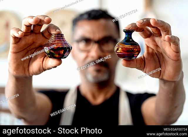 Close-up of male artist holding miniature vases in workshop