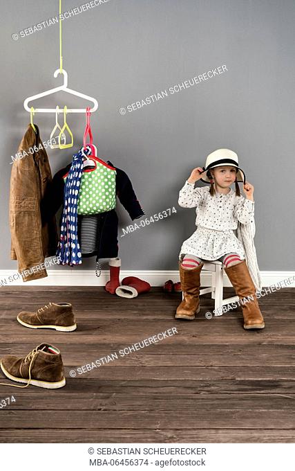 Girl sits on a chair in the wardrobe and wears the shoes of the mother