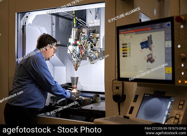 PRODUCTION - 30 November 2022, Baden-Wuerttemberg, Ditzingen: An employee of laser specialist Trumpf uses a model of a thruster for space shuttles to...