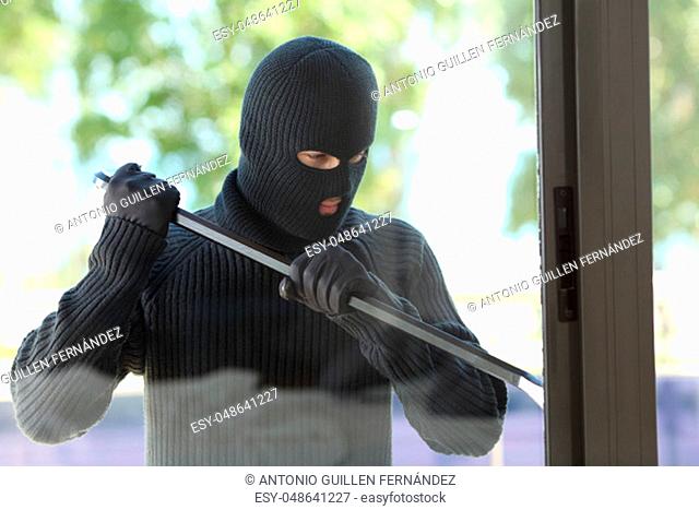 Thief wearing black mask trying to open a house window with a lever