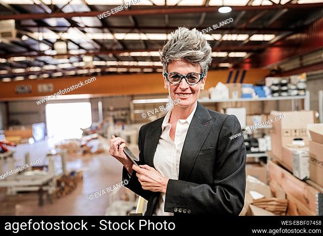 Happy mature businesswoman standing with tablet computer at industry