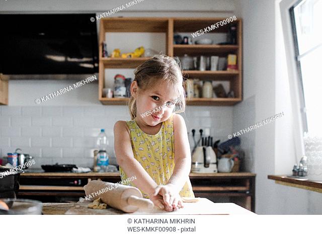 Portrait of smiling little girl kneading dough in the kitchen
