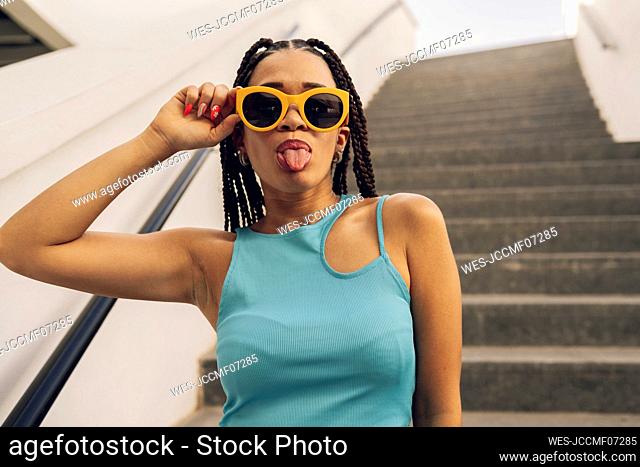 Young woman wearing sunglasses sticking out tongue on staircase