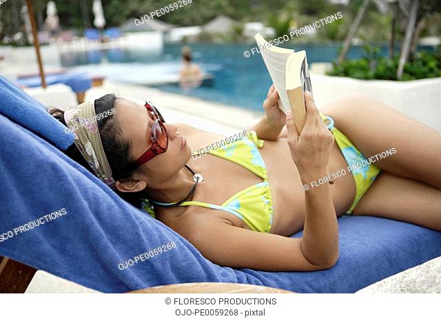 Woman lying by pool with book