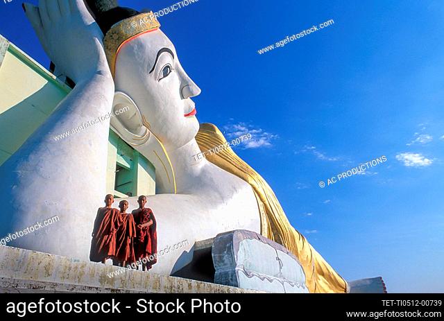 Myanmar, Monyma, Mandalay District, Novice monks standing under giant statue of reclining Buddha in Lay Kyune Sakkyar temple