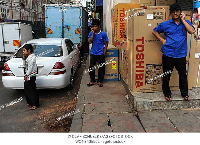 Yangon, Myanmar, Asia - Three people simultaneously talk on the phone on a sidewalk in front of a household supply store