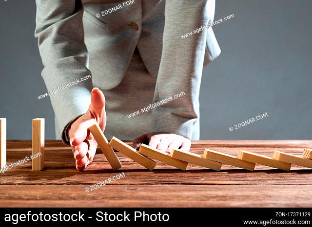 Close up female hand interrupting domino effect. Operative business solution, strategy and successful intervention. Business assistance concept with wooden...