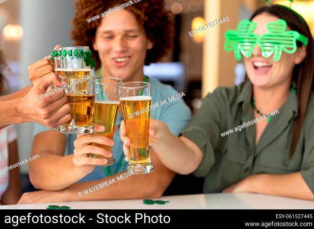 Diverse group of happy friends celebrating st patrick's day making toast with glasses of beer at bar