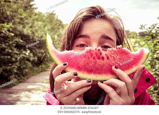 girl is holding a bitten slice of melon in front of here face, vintage color filter