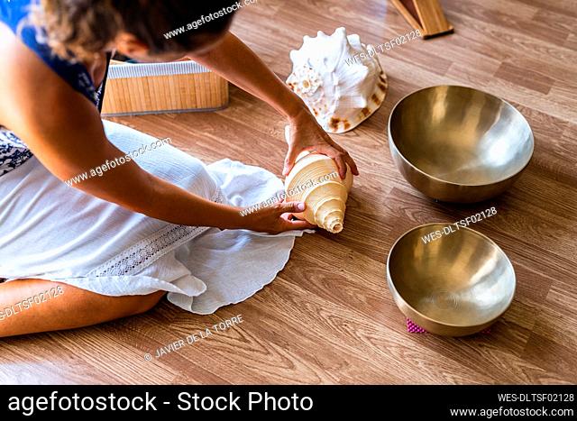 Female sound therapist with seashell sitting on hardwood floor