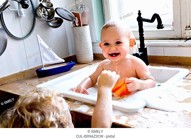 Boy playing with baby brother bathing in kitchen sink