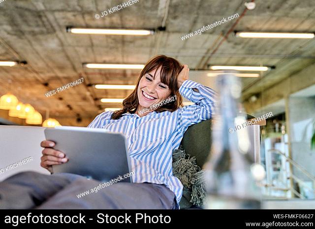 Smiling woman with hand in hands using digital tablet while sitting on sofa at home