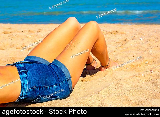 Young caucasian woman with short jeans sunbathes on beach near sea