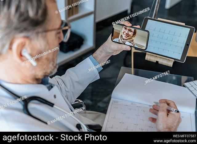 Mature doctor talking to female patient over mobile phone while sitting at doctor's office