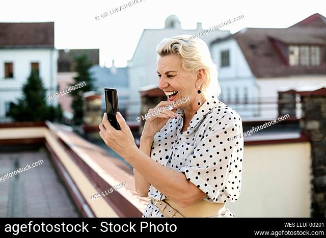 Happy woman attending video call through smart phone at building terrace