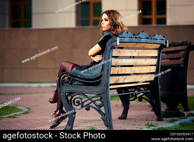 Sad young fashion woman with long curly hairs sitting on bench