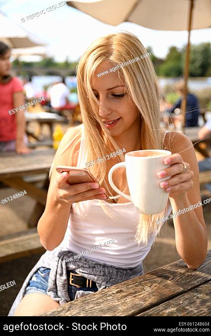 Portrait of young pretty woman in a street café with a cup of coffee latte in her hand and the London wind blowing into her hair in the United Kingdom