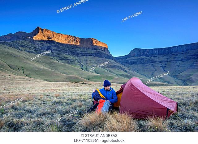 Man sitting in front of tent, Giant's Castle and Longwall in background, Giant's Castle, Drakensberg, uKhahlamba-Drakensberg Park