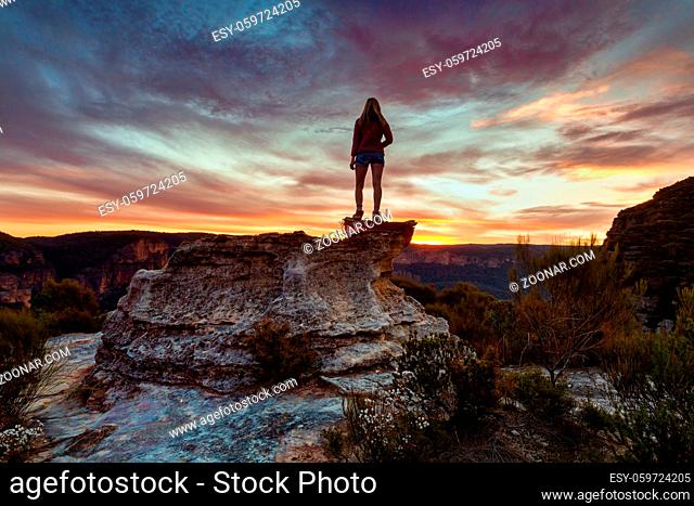 Hiker on podium like rock with wonderful views of the sandstone cliffs catching the last light of the setting sun in Blue Mountains